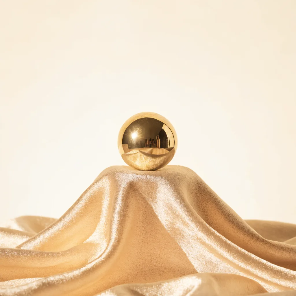 A single polished gold sphere in sharp focus on draped cream silk